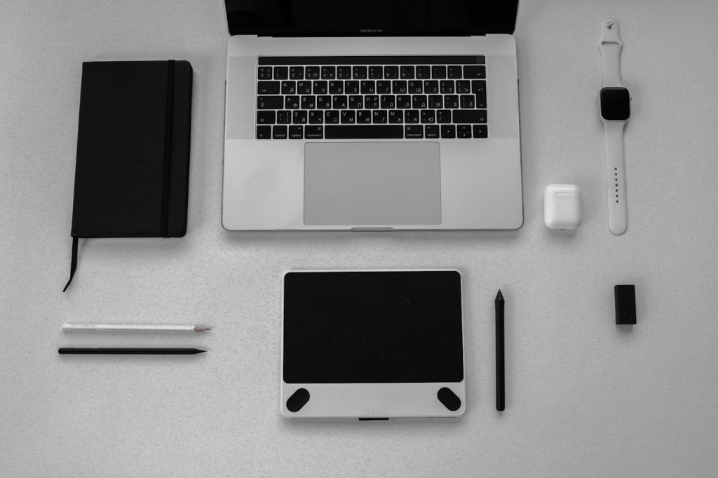 black-notebook-beside-a-macbook-pro-6192321 Black and white flatlay of stylish tech gadgets including laptop and smartwatch on a desk.